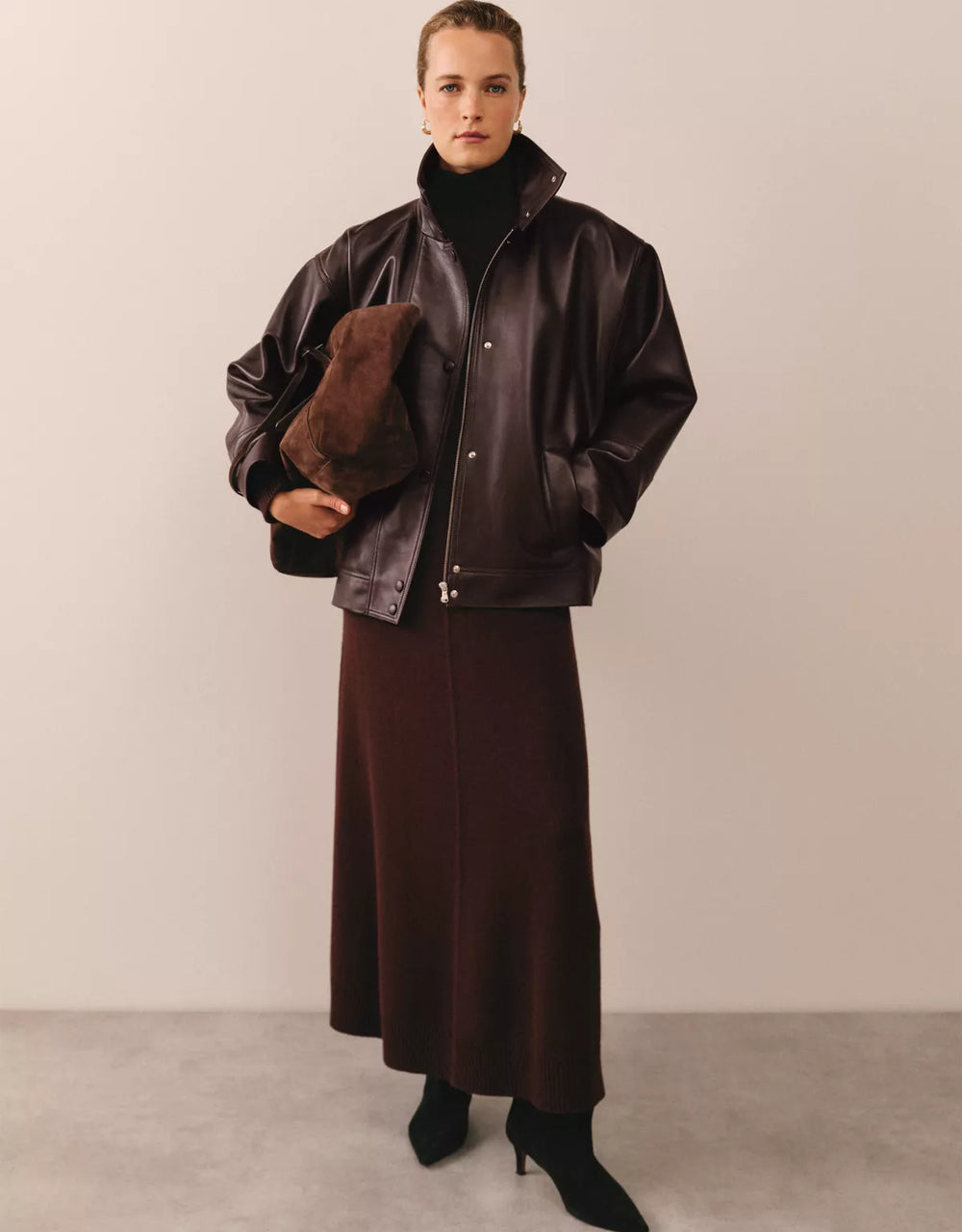 Dark leather jacket with broad sleeves, high neck, long visible front fastening and contained hem