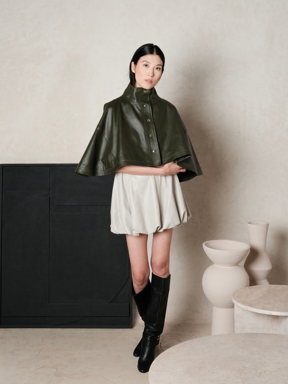 Short rounded cape with a high collar and front snaps, open lower edge around the arms.