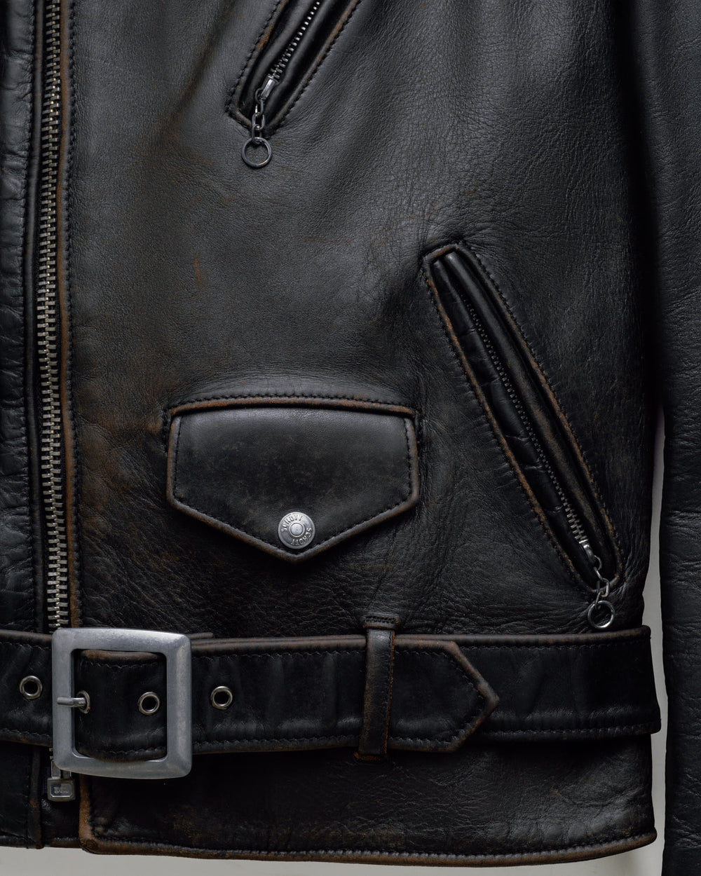 Black Schott jacket detail showing brown edges along a pocket, belt and hem.