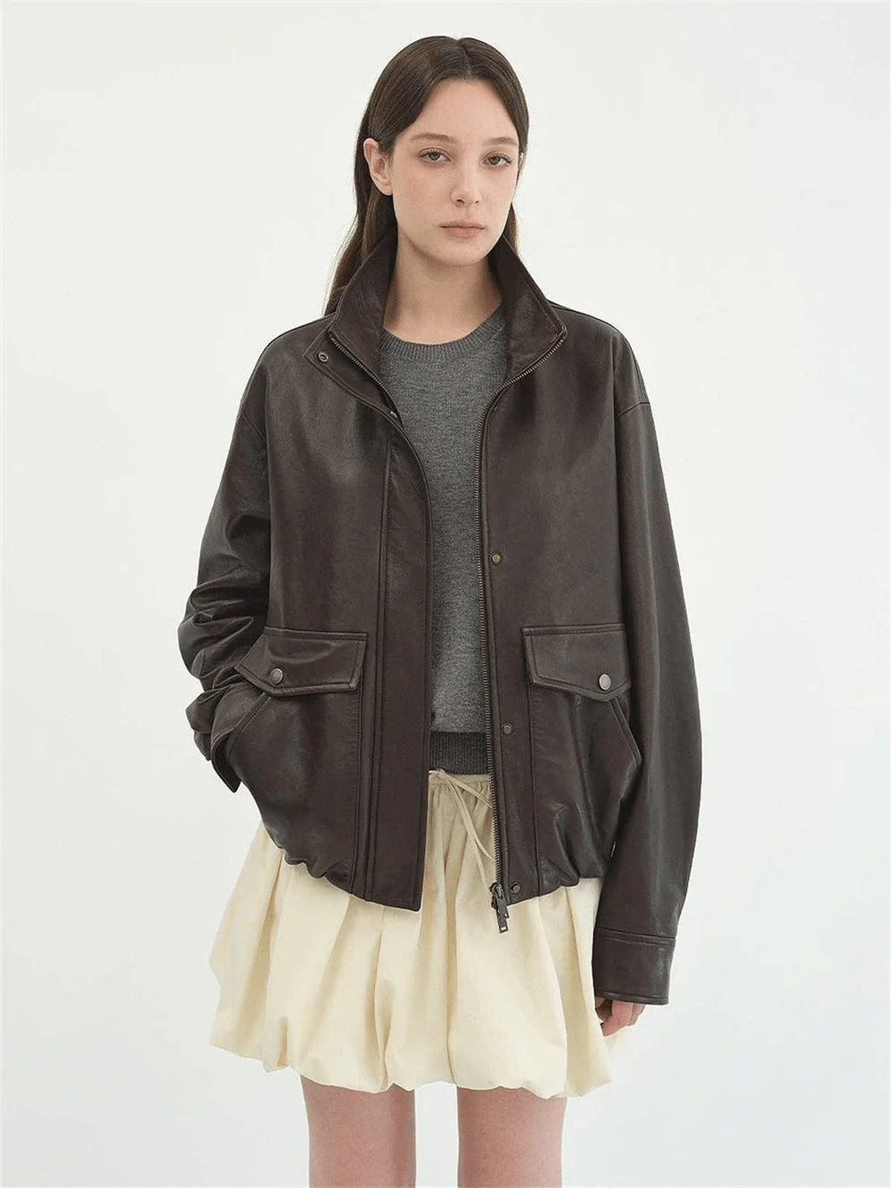 Brown cropped jacket worn open over a grey top and a pale short gathered skirt