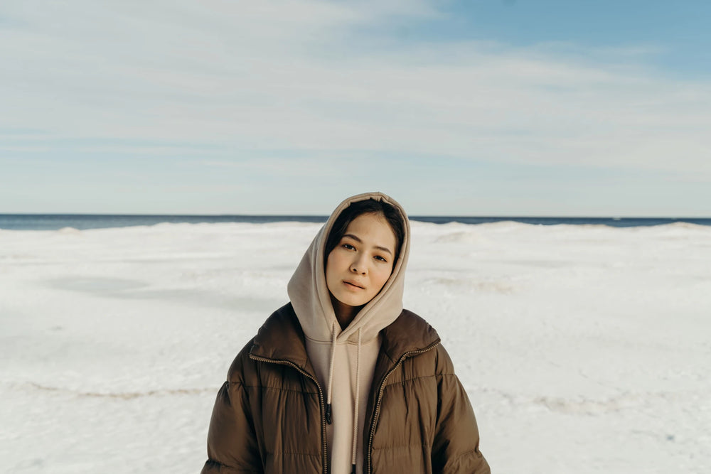 Woman in a brown quilted coat over a beige hooded top on a snowy coast
