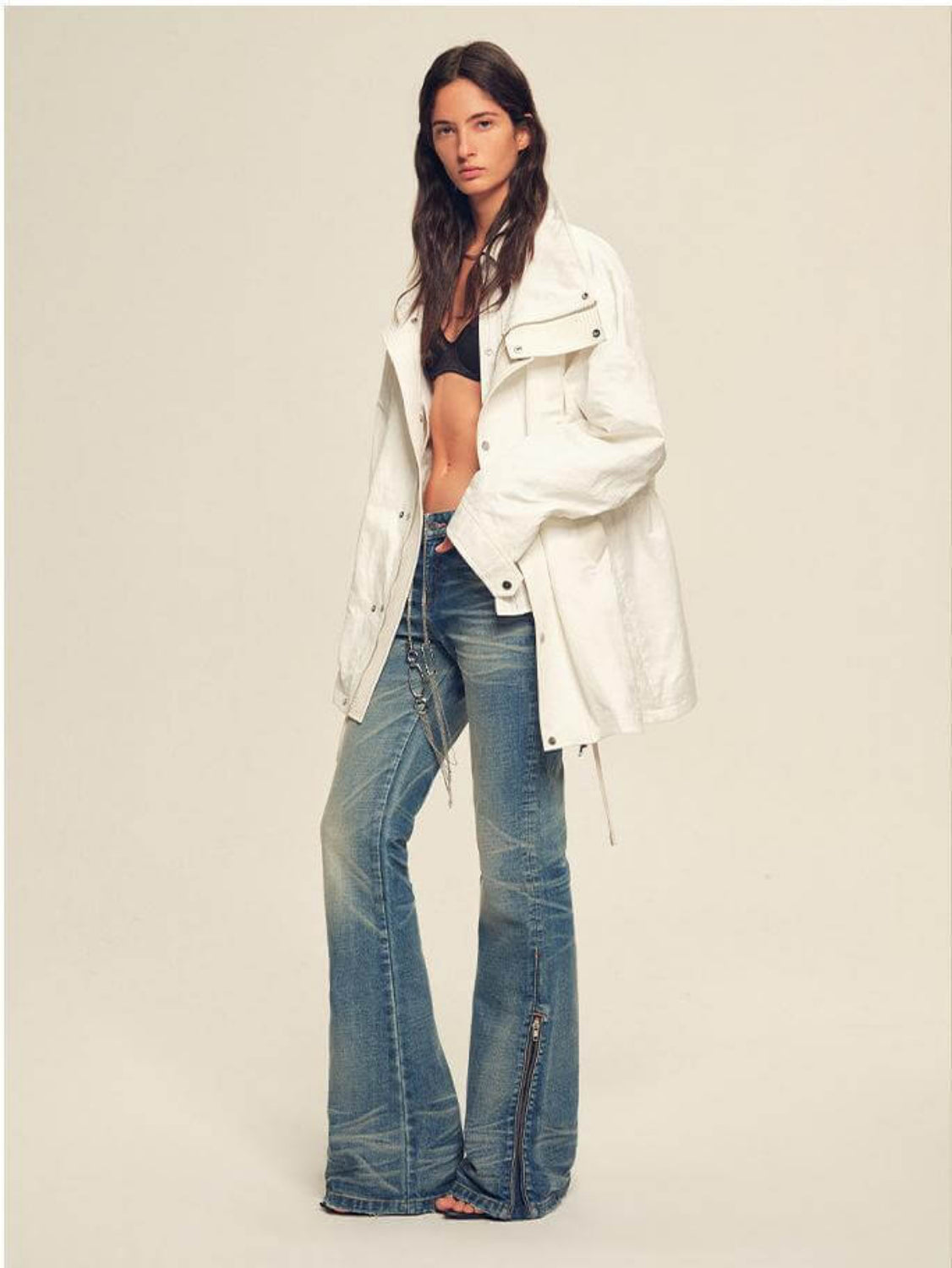 Woman wearing a white jacket and blue jeans on a plain background