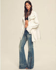 Woman wearing a white jacket and blue jeans on a plain background
